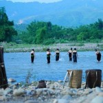 Young Thai girls in the river leave load of wood and back-baskets in the bank