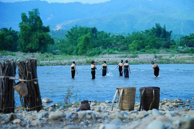 Young Thai girls in the river leave load of wood and back-baskets in the bank